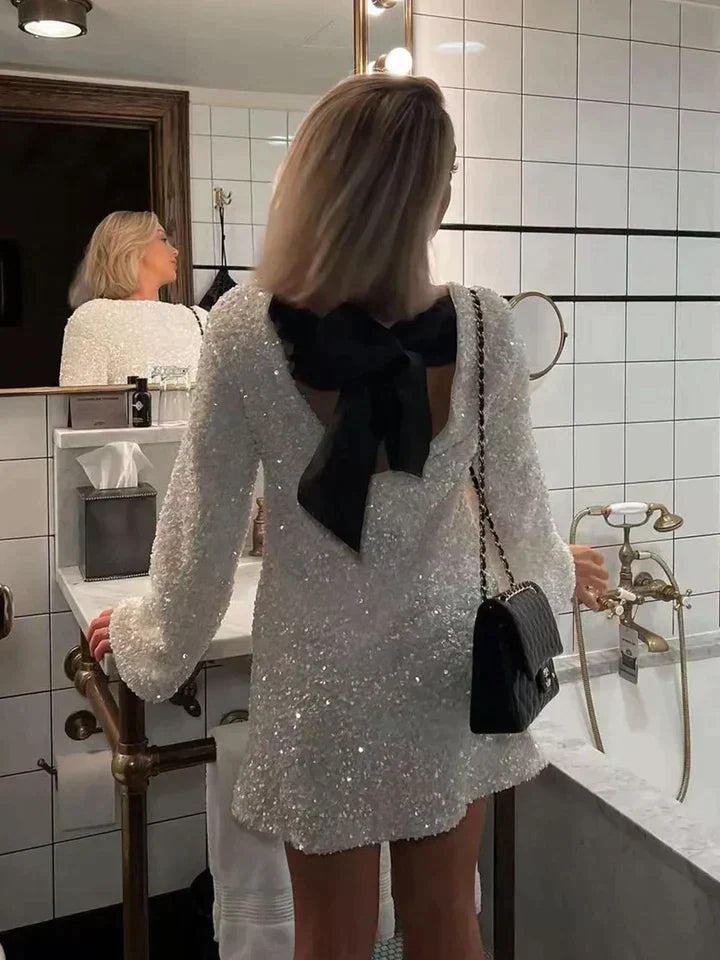 Frau im weißen Paillettenkleid mit schwarzer Schleife im Badezimmer, elegante Abendmode.