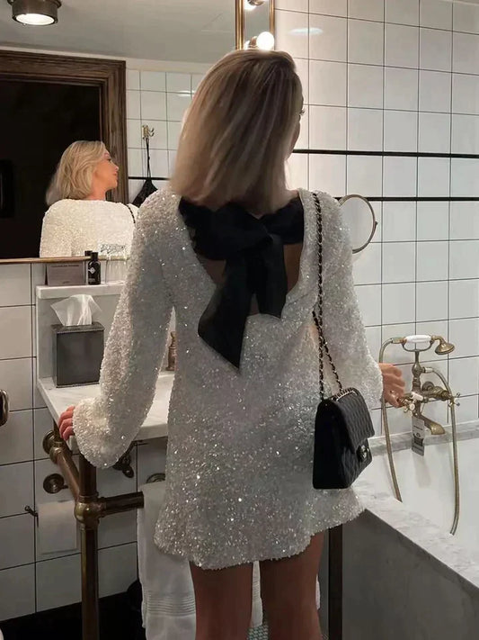 Frau im weißen Paillettenkleid mit schwarzer Schleife im Badezimmer, elegante Abendmode.