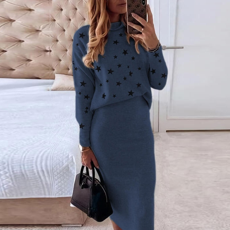 Frau in blauem Strickkleid mit Sternenmuster, hält schwarze Handtasche, modernes Schlafzimmer.