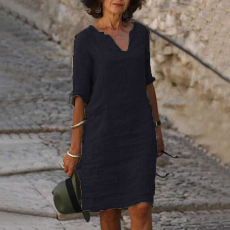 Frau in schwarzem Leinenkleid, V-Ausschnitt, auf Kopfsteinpflasterweg, Sommermode.