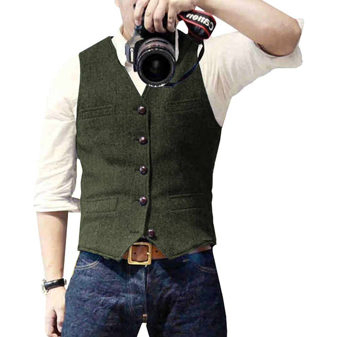 Mann in grünem Wollgilet mit Kamera, weißem Hemd und blauer Jeans.