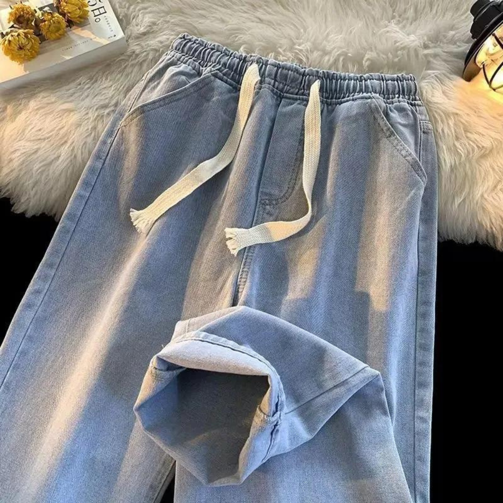 Hellblaue Jogginghose aus Denim mit Kordelzug, lässig, bequem, modisch, auf flauschigem Teppich.