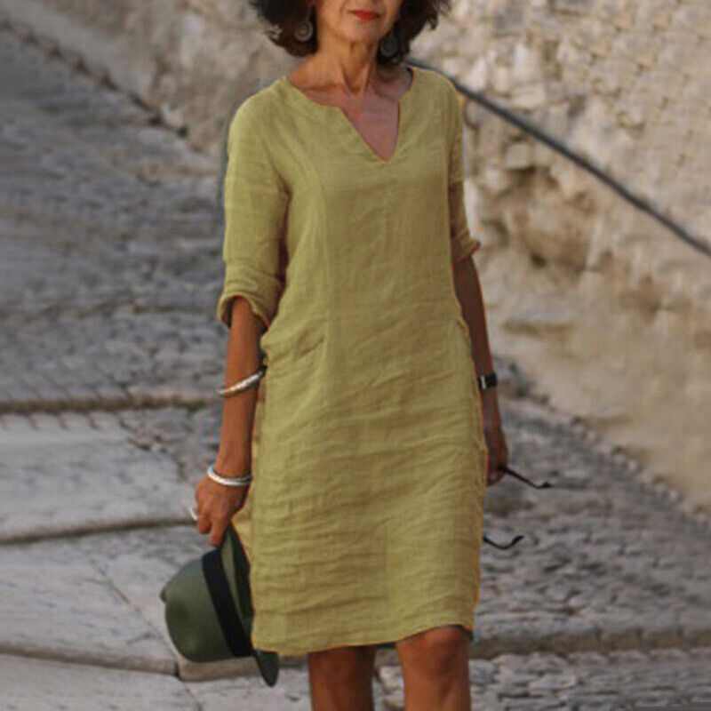Frau in gelbem Leinenkleid, V-Ausschnitt, auf Kopfsteinpflaster, Sommermode, lässiger Stil.