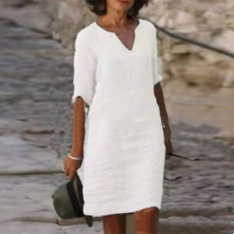 Frau in weißem Leinenkleid, knielang, mit V-Ausschnitt, Sommermode, lässiger Stil.