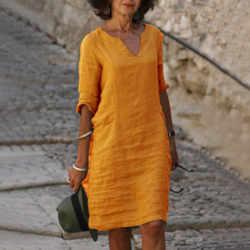 Frau in gelbem Leinenkleid, Sommermode, lässiger Stil, Spaziergang auf Kopfsteinpflaster.